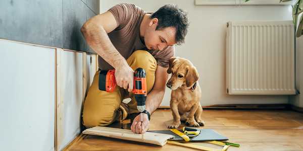 A man sitting next to a dog and drilling hole.